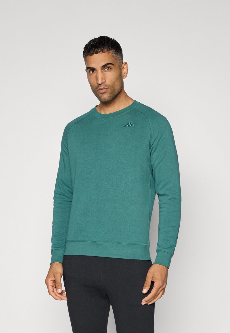 Teal crewneck sweatshirt met lange mouwen, geribbelde manchetten en zoom. Bevat een klein geborduurd logo op de linkerkant van de borst. Soepele textuur.