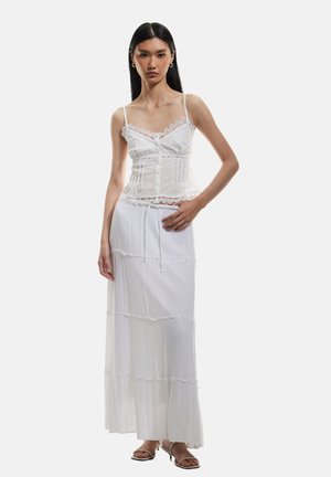 Witte cami-top met kantafwerking en dunne schouderbandjes, gecombineerd met een vloeiende, gelaagde witte maxirok. Zachte textuur, lichtgewicht stof.