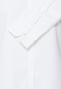 Poignet de chemise blanche à manches longues avec deux boutons blancs attachés, montrant un tissu propre et des détails de couture nets.