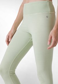 Vaaleanvihreissä legginsseissä on korkea, ribattu vyötärö ja sileä pinta, ja sivussa on hienovarainen logoyksityiskohta sekä kontrastiväriset saumat.