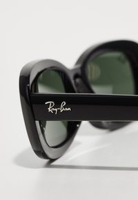 Ochelari de soare negri Ray-Ban cu lentile rotunde, nuanță verde, ramă din plastic lucios și logo argintiu pe lateral. Design distinctiv supradimensionat.