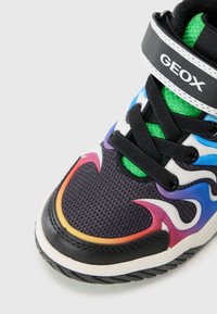 Zwart-witte sneaker met een meerkleurig vlammotief, mesh bovenkant, groene accenten en zwarte veters. Beschikt over een gewatteerde kraag en een gelabelde strap.
