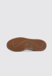 Suola in gomma per sneaker con motivo a spina di pesce, con logo Puma. Il colore è marrone, con una trama liscia e linee curve.