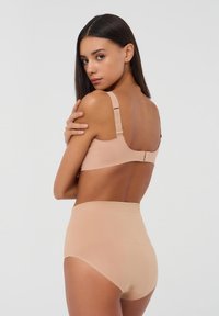 Reggiseno color nude con spalline regolabili e chiusura a gancio, abbinato a mutande alte color nude con una texture liscia e senza cuciture.