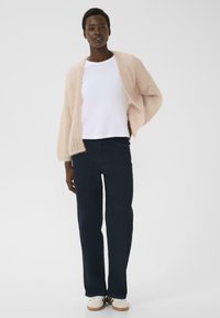 Lys rosa strikket cardigan, hvid T-shirt, mørke denim jeans, modellen står afslappet. Cardiganen har en løs pasform og blød tekstur.
