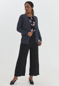 Cárdigan de punto en color navy sobre una blusa negra con flores, combinado con pantalones sueltos negros y tacones altos, con un ajuste relajado y un diseño de frente abierto.