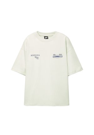 Světle zelené oversized tričko vyrobené z bavlny, s grafickými potisky v tmavě modré barvě na přední straně, s kulatým výstřihem a krátkými rukávy.