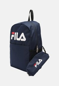 Zaino Fila di colore blu navy realizzato in tessuto resistente, con tasca frontale con zip, tasca laterale in rete e grande logo bianco sul davanti.