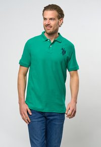 Zelená polo košeľa s golierom, krátkymi rukávmi a námorníckym logom koňa na ľavej hrudi. Vyrobená z textúrovanej bavlnenej látky.