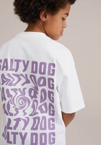 Bílý bavlněný tričko s fialovým grafickým designem a nápisem "SALTY DOG" napsaným různými stylizovanými fonty na zadní straně.