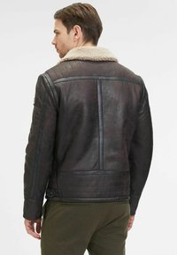 Giubbotto in pelle marrone con colletto in shearling, caratterizzato da una texture liscia, design trapuntato sul retro e silhouette aderente.