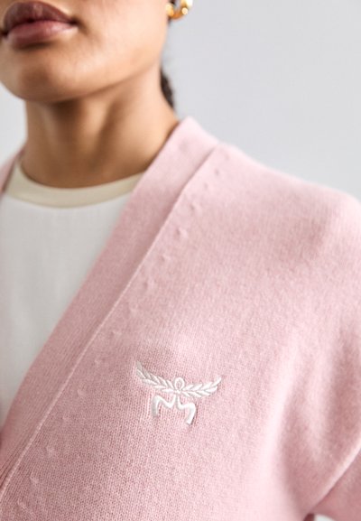 Roze gebreide cardigan met een V-hals, voorzien van een witte geborduurde logo op de borst en een gestructureerde afwerking langs de randen.