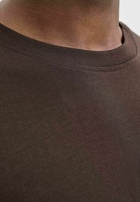 Brun bomulds t-shirt med rund hals, der har en glat tekstur og fine ribbede detaljer ved halsen. Nærbillede, der fremhæver syningerne.