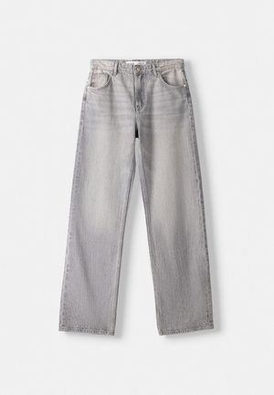 Femme portant un débardeur court blanc, un jean droit taille haute gris clair et des baskets blanches avec des semelles en gomme.