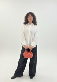 Biela košeľa s golierom, čierne široké nohavice a malá koralová kabelka so sťahovacou rúčkou. Celkovo hladké textúry látky.