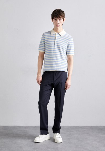 Korte ermel polo skjorte i lyseblå og kremfargede striper; ribbestrikket tekstur; knappetar. Kombinert med mørke bukser og hvite sneakers.