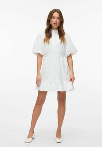 Witte jurk met pofmouwen, knopen aan de voorkant en kanten details. Uitlopende zoom met een gerimpelde rand. Gekocht met bijpassende lichtgekleurde schoenen.