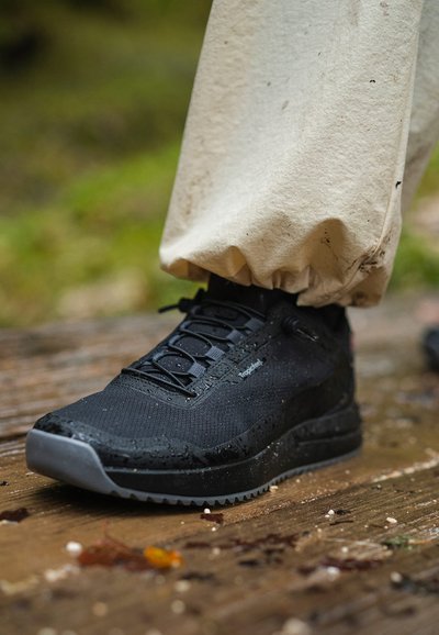 Black athletic shoe with a textured surface, waterproof material, and rubber sole. Features elastic laces and a sleek design.