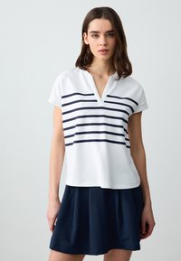 Weißes Kurzarmoberteil mit marineblauen horizontalen Streifen, V-Ausschnitt-Design, kombiniert mit einem dunkelblauen plissierten Rock. Glatte Stoffoberfläche.