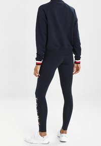 Námořnicky modrý set mikiny a legín, s žebrovanými lemy s červenými a bílými akcenty. Legíny mají podél strany vícebarevné logo "TOMMY".