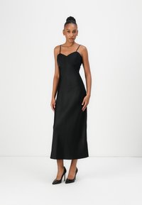 Black satin long dress with a fitted bodice, thin straps, and a flowing skirt. Worn with black high-heeled shoes. Smooth texture and minimalist design.