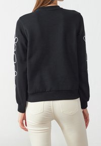 Svart sweatshirt med ribbade mudd och fåll, prydd med vit grafisk design på båda ärmarna, tillverkad av mjukt, strukturerat tyg.