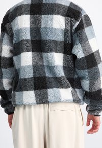 Fleecetröja i svart, vitt och ljusblått rutig mönster. Har en mjuk, texturerad yta med en lös passform och långa ärmar.