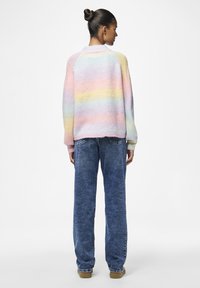 Pastel gestreepte trui met een ronde hals, gebreide textuur en een oversized pasvorm, gecombineerd met loszittende blauwe denim jeans en bruin schoeisel.