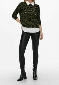 Olivgrön tröja med svart leopardtryck, vit krage under, ihop med svarta syntetiska skinnleggings och svarta klackstövlar.