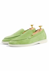 Zapatos verdes de ante tipo slip-on con punta redondeada, detalles de costura y suelas de goma blanca. Textura suave, con árboles para zapatos de madera.