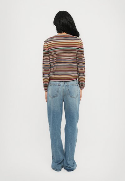 Top a maniche lunghe a righe in vari colori abbinato a jeans in denim azzurro chiaro a vita alta. Entrambi hanno una vestibilità rilassata e uno stile casual.