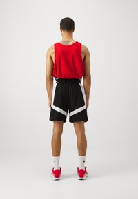 Red sleeveless athletic top, black shorts with white diagonal accents, white socks, and red athletic shoes. Back view with minimal detail.