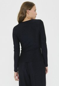 Dlhý rukáv, priliehavý top v čiernej farbe s jemným leskom. Má zaoblený výstrih a hladkú, textúrovanú tkaninu.