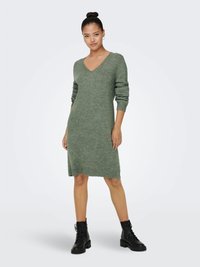 Abito in maglia di colore verde tenue, con scollo a V e maniche lunghe, finitura a costine. Abbinato a stivali neri con lacci alla caviglia.