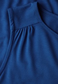 Niebieski bezrękawnik z marszczonym detalem na ramieniu. Wykonany z gładkiego, elastycznego materiału z czystym dekoltem i wykończonymi krawędziami.