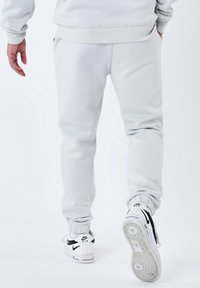 Lichtgrijze joggers met elastische boorden, zijzakken en geribde tailleband, gecombineerd met witte Nike sneakers met zwarte accenten.