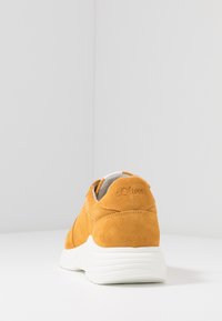 Yellow suede sneaker with perforated detailing, white rubber sole, and subtle logo accent on the heel. Smooth texture and rounded shape.
