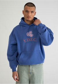 Blå hoodie med oversized pasform, prydet med en pink blomstret grafik og teksten "Y.D.F.C." på brystet. Blødt bomuldsmateriale med en frontlomme.