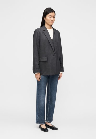 Blazer gris à fines rayures avec un col cranté, coupe oversize, associé à un jean bleu taille haute et des chaussures plates noires.