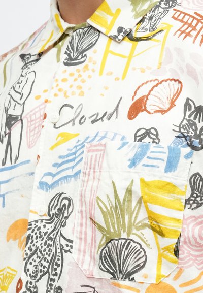 Μπλούζα με κοντά μανίκια από πολύχρωμο, υφασμάτινο ύφασμα με υφή που παρουσιάζει διάφορες εικονογραφήσεις, όπως κοχύλια, φυτά και φιγούρες, σε πολλές αποχρώσεις.