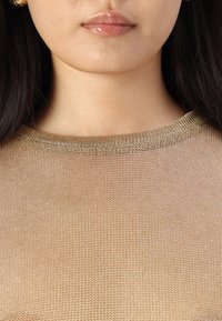 Gullmetallisk strikket topp med rund hals, med en fin nettstruktur som lar lys slippe gjennom og fremhever huden under.