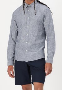 Lichtblauw overhemd met knoopsluiting, gemaakt van textuurstof, met een gespreide kraag, lange mouwen en knoopsluiting, gecombineerd met marineblauwe shorts.