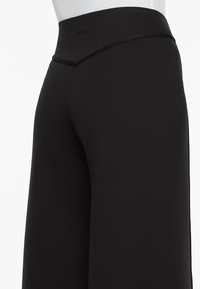 Schwarze, weite Hose aus dehnbarem Material. Merkmale einen hohen Taillenbund mit glatter Oberfläche und ohne sichtbare Verschlüsse oder Verzierungen.