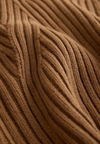 Gros plan sur un tissu tricoté côtelé marron doux avec des lignes verticales texturées visibles et des plis.