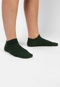 Grønne ankelstrømper lavet af et blødt, strækbart materiale med en ribbet kant. Designet er enkelt og glat, der dækker foden uden mønstre.