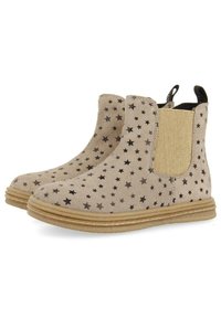 Botines beige de ante con un patrón de estrellas negras, paneles laterales elásticos y un acento dorado texturizado. Punta redondeada y suela de goma.