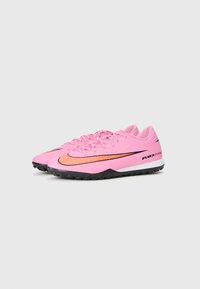 Scarpe da allenamento Nike rosa con una tomaia testurizzata, suola in gomma nera e dettagli arancioni. Presentano un design snellito e un sistema di allacciatura.