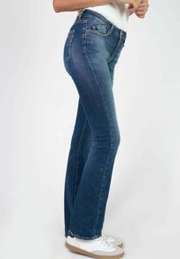 Donkerblauwe flared jeans van denim, met een klassiek vijf-pocket ontwerp, een middelhoge taille en subtiele vervaging. Gecombineerd met witte sneakers.