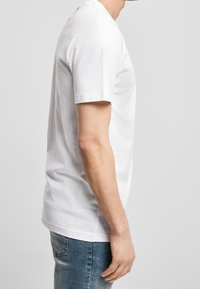 Bílé tričko s krátkým rukávem vyrobené z bavlny, s kulatým výstřihem a volným střihem, v kombinaci s modrými džíny. Jednoduchý design bez vzorů.