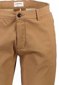 Slim-fit, tanbyxor tillverkade av slät tyg. Har en knappstängning, sidofickor och subtila sömmar. Etikett synlig vid midjan.